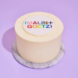 Corporate White Iced Cake with Logo featuring smooth white icing and a colorful edible logo plaque on top.
